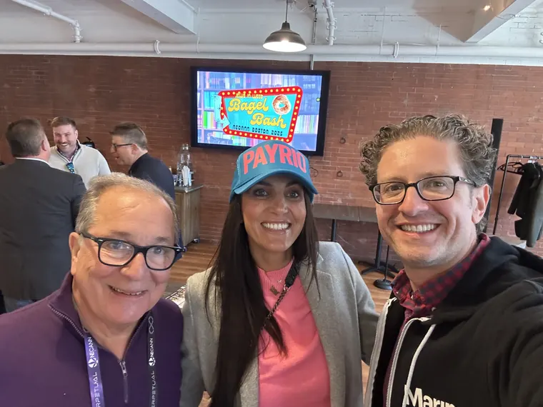 Jordan Isenstadt with two guests, one in a PayRio cap, under the Bagel Bash sign