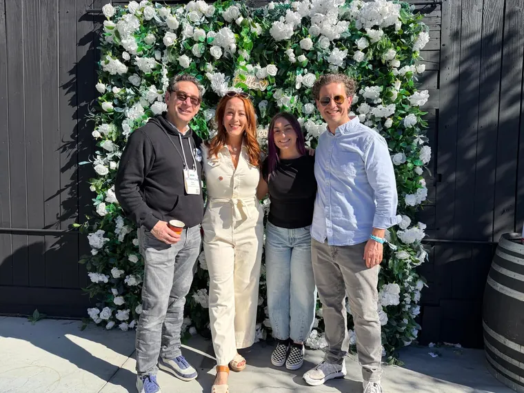 Four guests posing in front of a white flower wall at the Ventura Bagel Bash