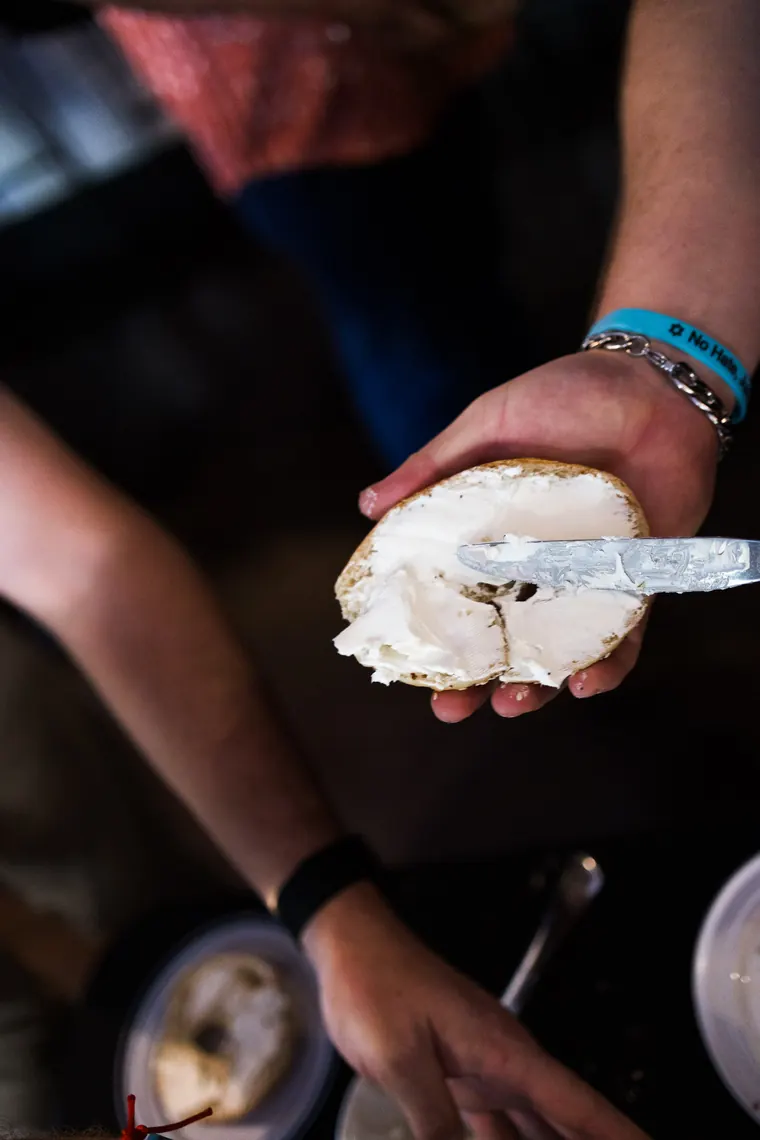 Close-up of a hand spreading cream cheese on a bagel