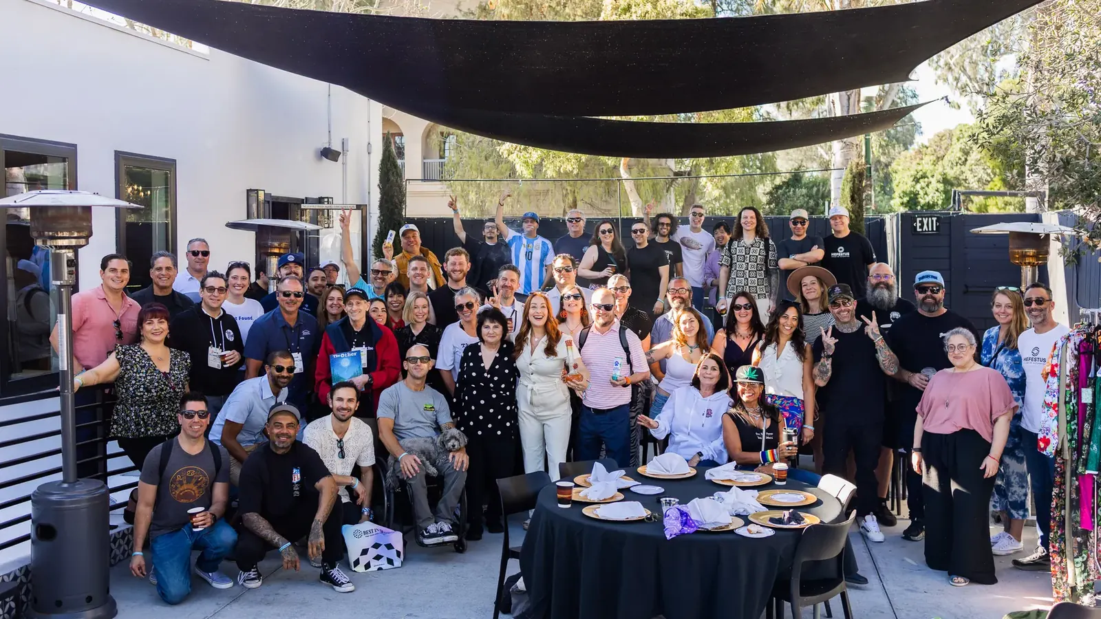 The Hall of Flowers Bagel Bash crowd gathered for a group photo under black shade sails on the White House Beach Club patio